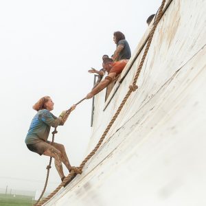 Mulher segurando em corda para tentar escalar rampa na Tough Mudder